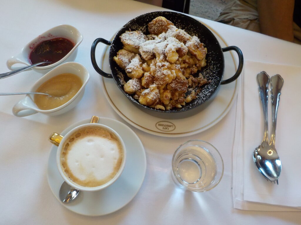This picture shows the Austrian dessert "Kaiserschmarrn" with 2 sauces on the side: apple sauce and plum sauce. On the table there is also a cup of coffee.