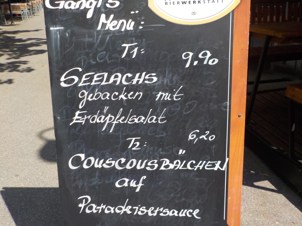 This picture shows a restaurant sign with today's specials (Menü): the two options are Lachs mit Salat oder Couscousbällchen mit Suppe.