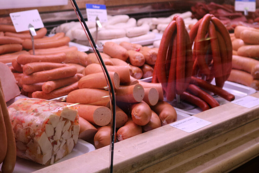 This picture shows a sausage stand at a market with a display of several different kinds of sausage.