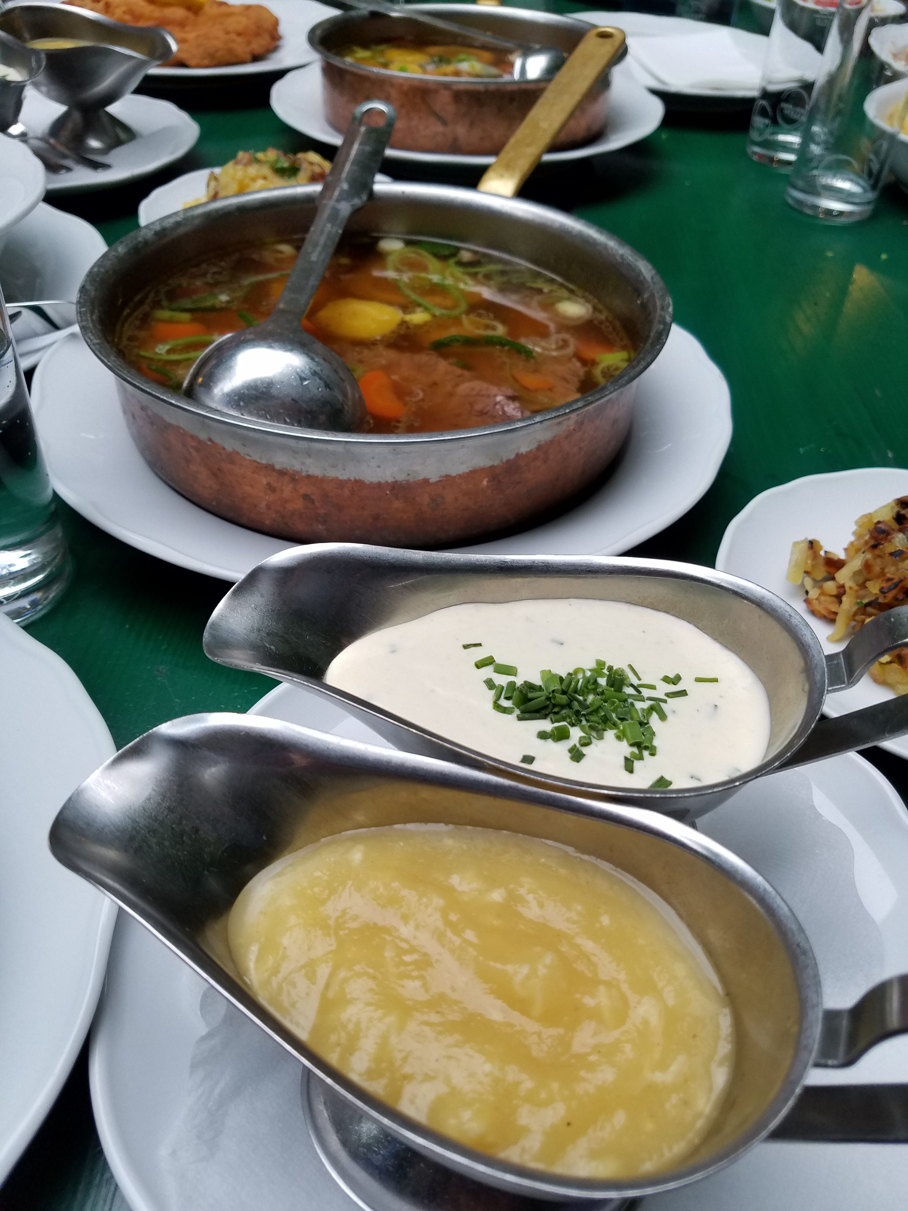 Austrian culinary specialty. A pot of vegetable broth with a spoon in it sits on a table next to two gravy boats filled with sauces. Beef or veal is typically cooked in the broth and then served in the pot with sauces on the side.