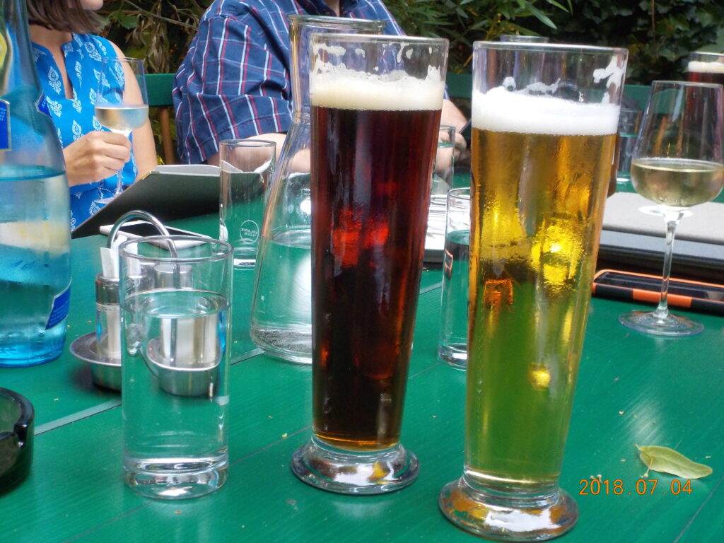 This picture shows several drinks on a table. Pictured are wine glasses, beer glasses, and a water glass and a water bottle.
