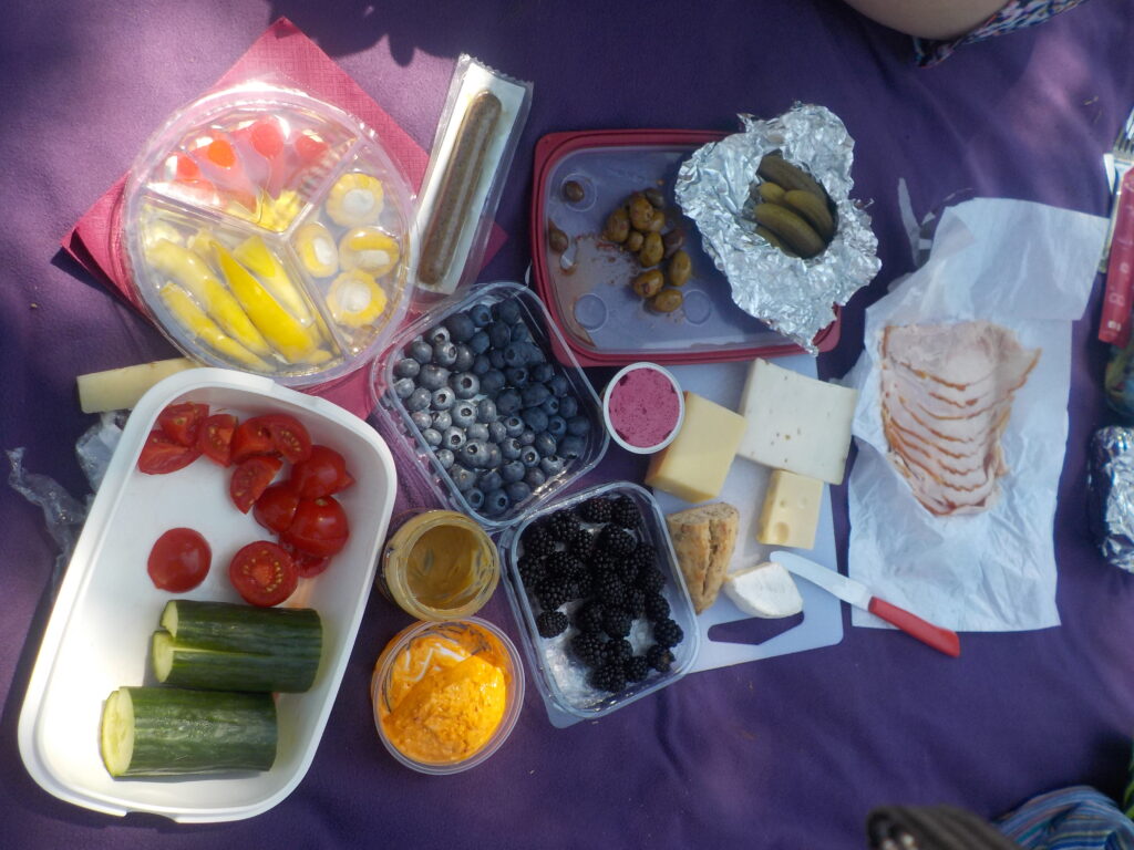 Picnic spread of tomato and cucumber, black and blue berries, cheese, bread, and ham