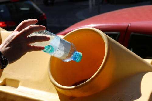 A decorative photo depicts a hand placing a used plastic water bottle into a public recycling bin.