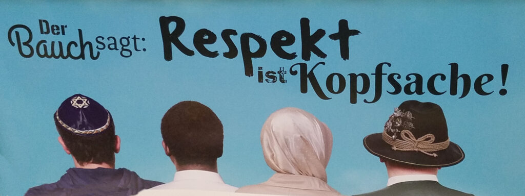 Subway ad showing four heads, one uncovered, one in a Jewish kippah, one in a Muslim headscarf or hijab, and one in a traditional Tirolean hat, reading "Der Bauch sagt, Respekt ist Kopfsache."