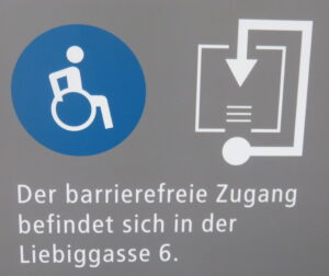 sign indicating the wheelchair accessible entrance to a university building is around the corner