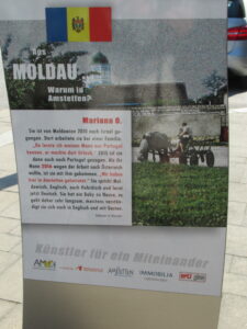 "Menschen aus aller Welt daheim in Amstetten" poster: full text of poster is included as the reading text for Moldova below. An image of an old stone farmhouse and farmers working in a field using a horse-drawn cart.
