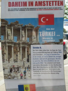 "Menschen aus aller Welt daheim in Amstetten" poster: full text of poster is included as the reading text for Turkey below. An image of the Turkish flag and ancient Turkish ruins.