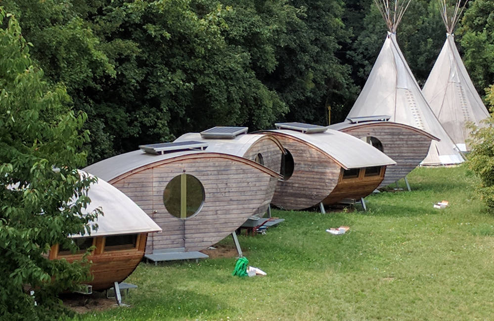 several tiny houses of wood in front of two white tipis